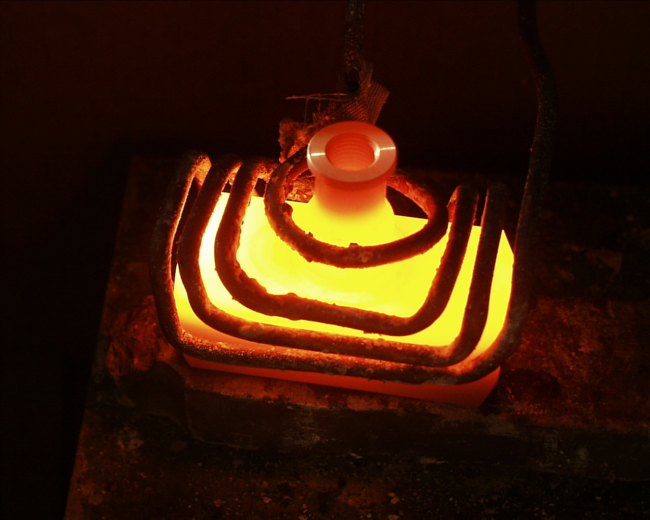 Glühendes Metallteil innerhalb mehrerer wassergekühlter Induktorwindungen