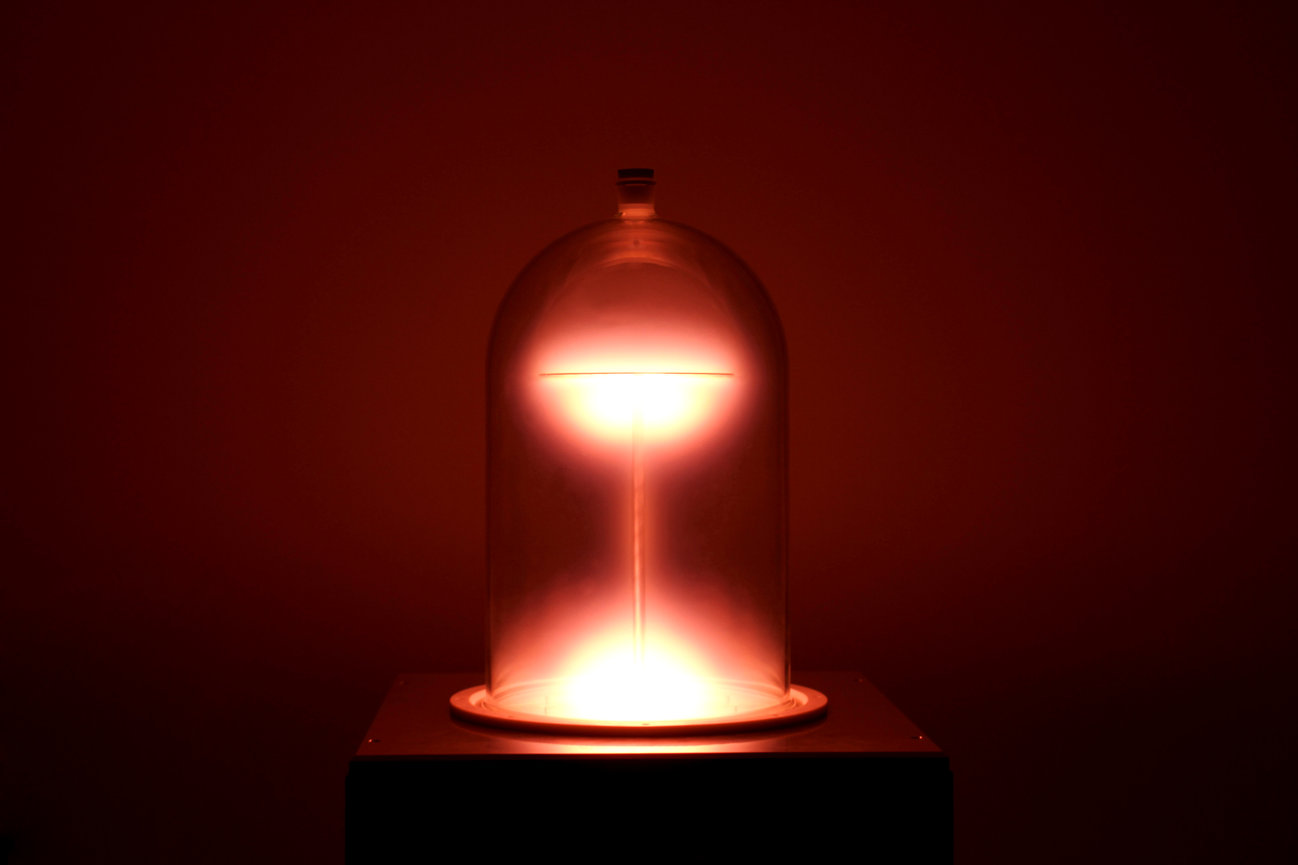 Leuchtende Entladung in einer gläsernen Bell-Jar-Glocke auf einer dunklen Grundplatte.