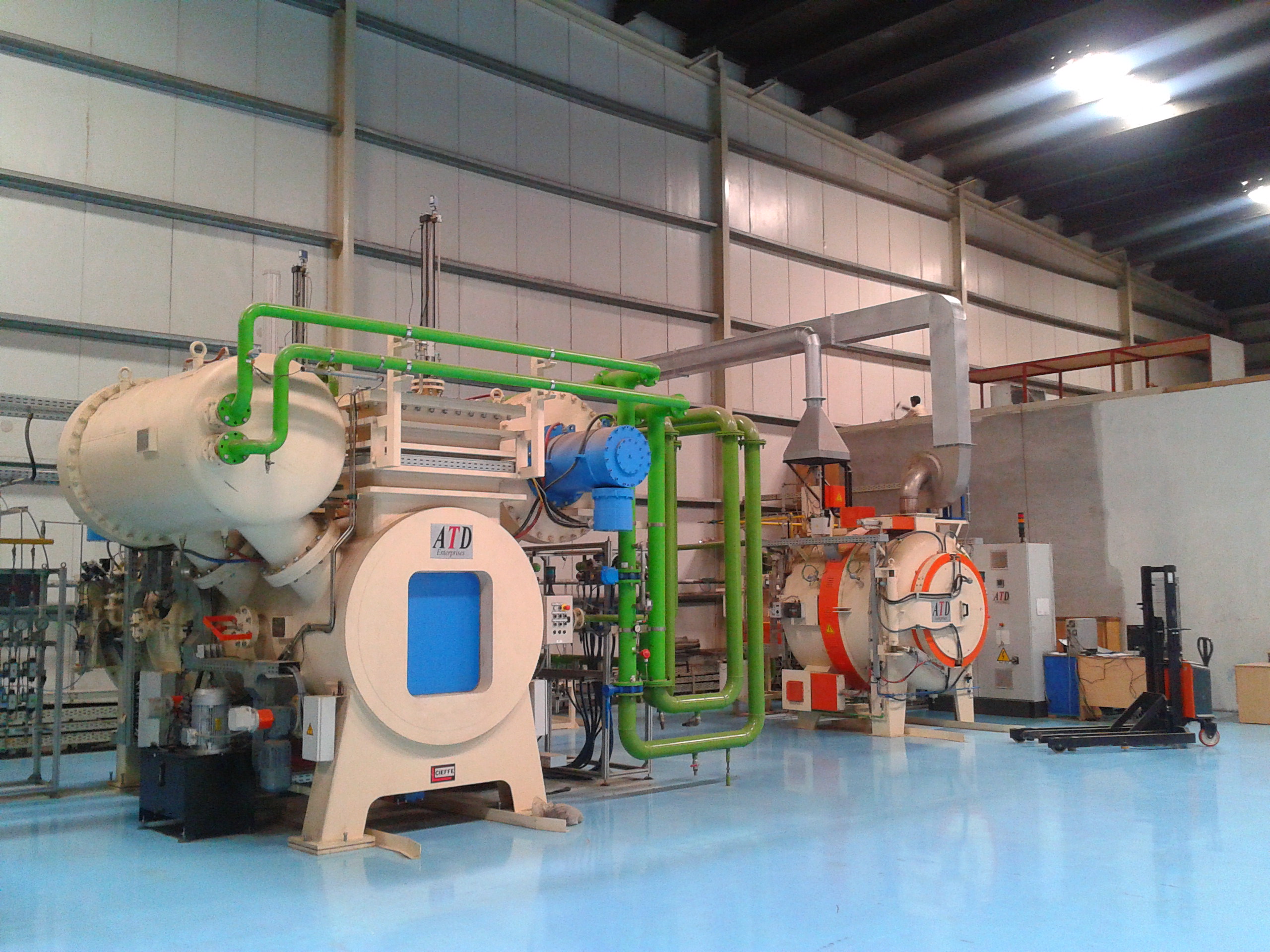 Historical heat-treatment furnaces with pale chambers, blue doors and green pipes in a workshop.
