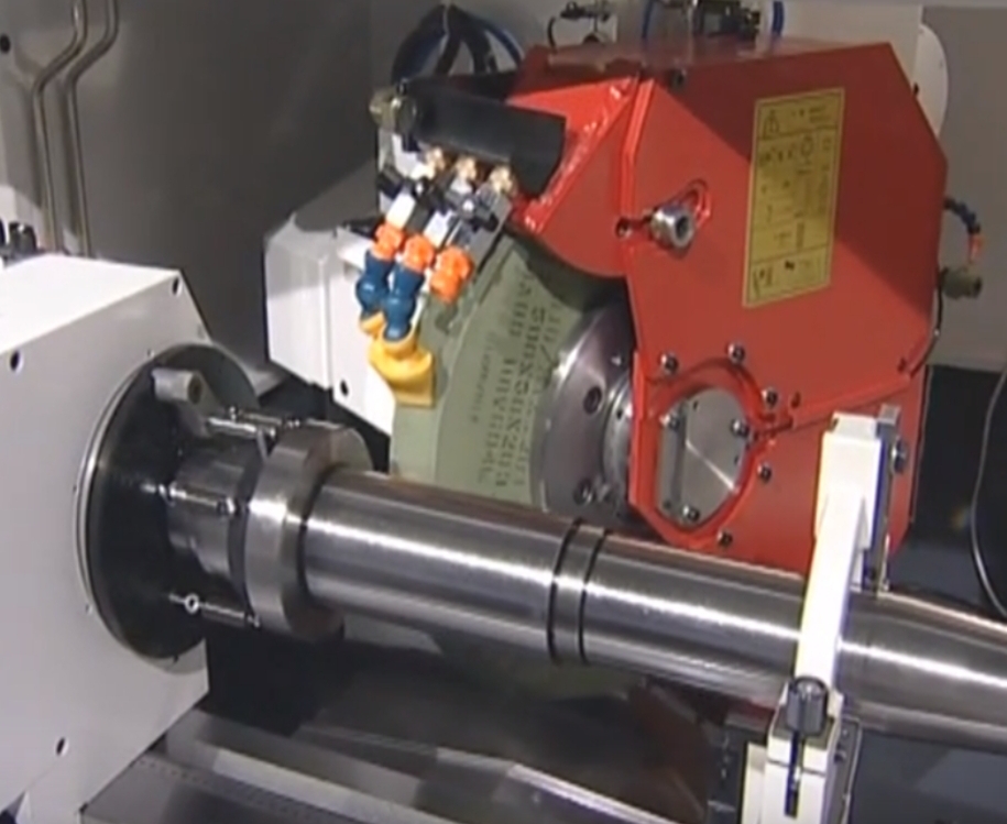 Rundschleifmaschine mit eingespanntem zylindrischem Werkstück, Schleifscheibe und Kühlmitteldüsen.